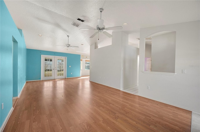 unfurnished living room featuring lofted ceiling, a textured ceiling, light hardwood / wood-style floors, and french doors