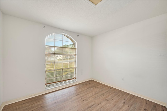 empty room with a textured ceiling and light hardwood / wood-style flooring