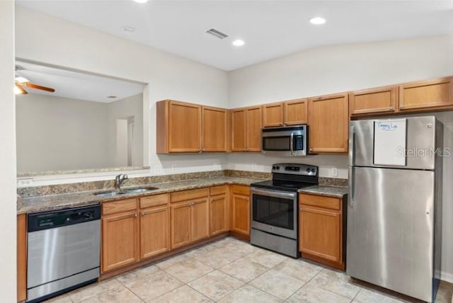 kitchen with sink, ceiling fan, appliances with stainless steel finishes, light tile patterned flooring, and dark stone counters