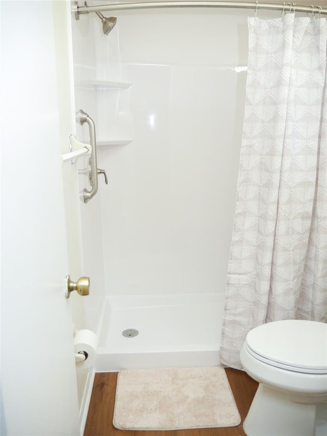 bathroom with wood-type flooring, toilet, and a shower with shower curtain