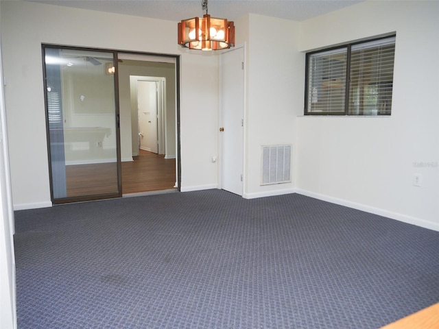 empty room with a notable chandelier and dark carpet