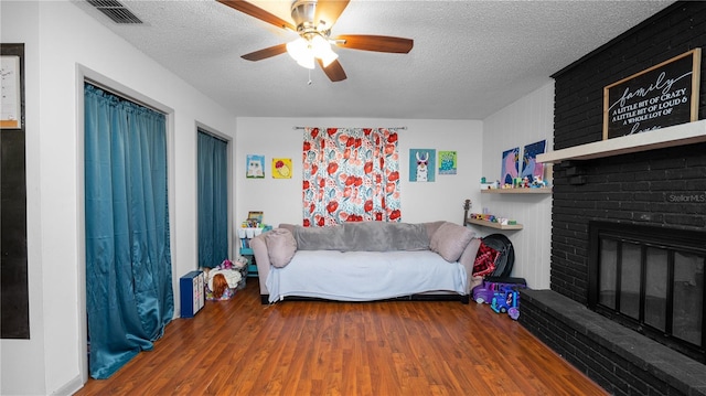 living room featuring ceiling fan, a brick fireplace, hardwood / wood-style floors, and a textured ceiling