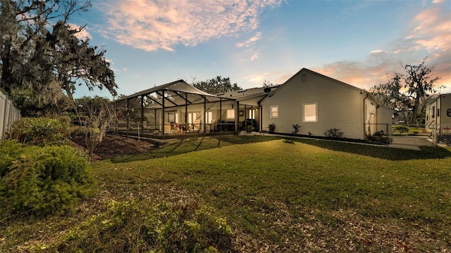 back house at dusk with a lanai and a lawn