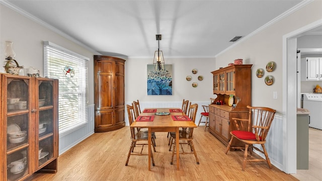 dining space featuring washer / dryer, ornamental molding, and light wood-type flooring