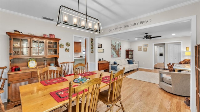 dining space with crown molding, ceiling fan with notable chandelier, and light wood-type flooring