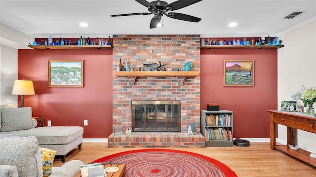 living room featuring hardwood / wood-style floors, a fireplace, ornamental molding, and ceiling fan