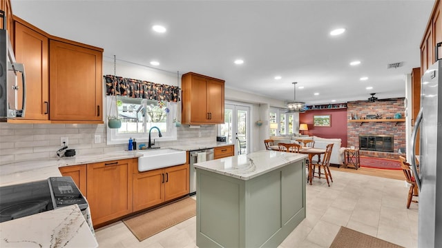 kitchen with sink, stainless steel appliances, light stone counters, a fireplace, and a kitchen island