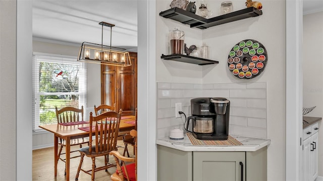 interior space featuring crown molding, pendant lighting, backsplash, and light hardwood / wood-style flooring