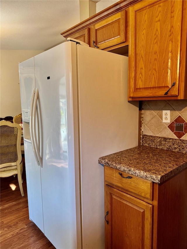 kitchen with white refrigerator with ice dispenser, brown cabinetry, and backsplash