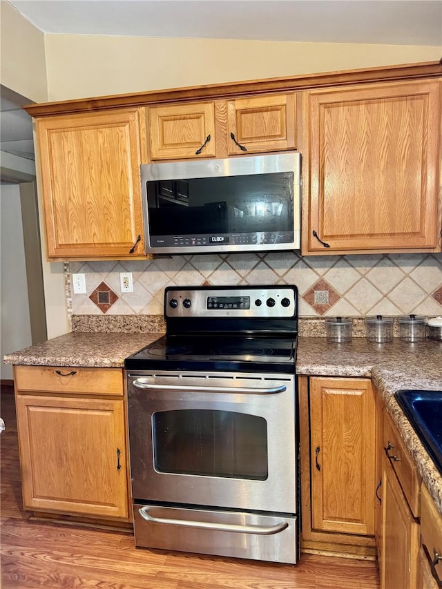 kitchen with backsplash, light hardwood / wood-style floors, and appliances with stainless steel finishes