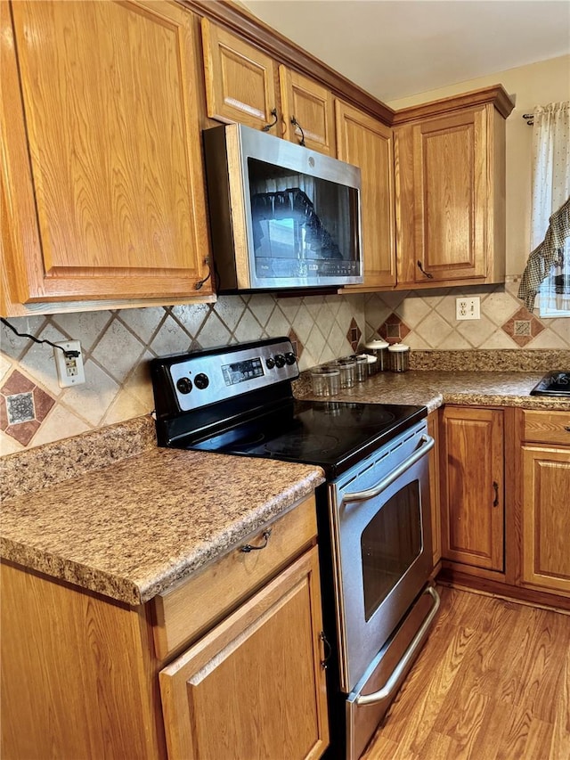 kitchen featuring stainless steel appliances, brown cabinets, light wood-style flooring, and decorative backsplash