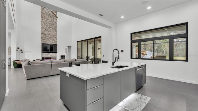 kitchen featuring sink, gray cabinetry, dishwasher, an island with sink, and a fireplace