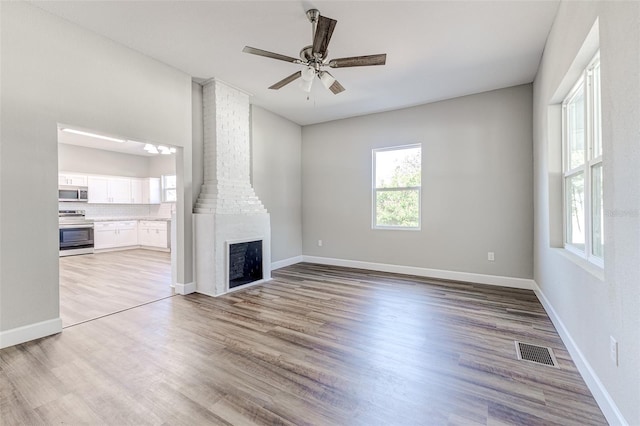 unfurnished living room with ceiling fan, a fireplace, and light hardwood / wood-style flooring