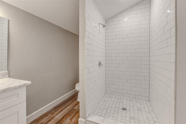 bathroom featuring toilet, wood-type flooring, vaulted ceiling, a tile shower, and vanity