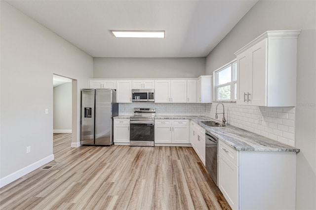 kitchen with sink, stainless steel appliances, tasteful backsplash, light stone countertops, and white cabinets