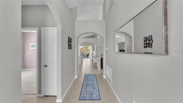 corridor with light tile patterned floors, visible vents, arched walkways, and baseboards