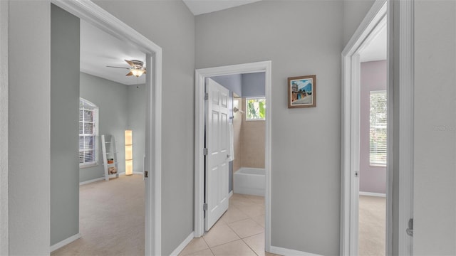 corridor featuring light tile patterned flooring, baseboards, and light carpet