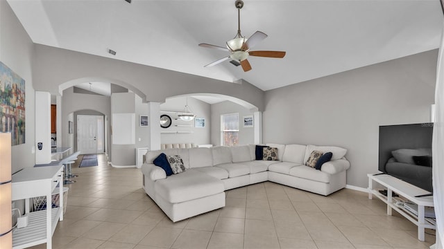 living area featuring a ceiling fan, arched walkways, light tile patterned flooring, baseboards, and vaulted ceiling