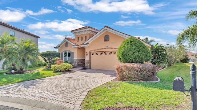 mediterranean / spanish-style house with a front yard, stucco siding, decorative driveway, stone siding, and an attached garage