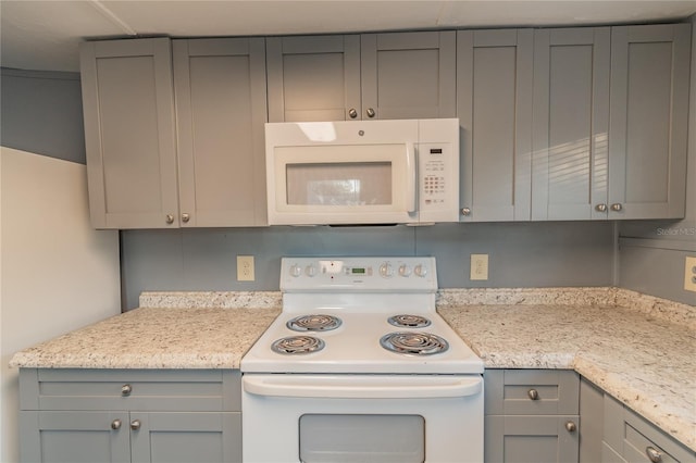 kitchen with light stone countertops, white appliances, and gray cabinetry