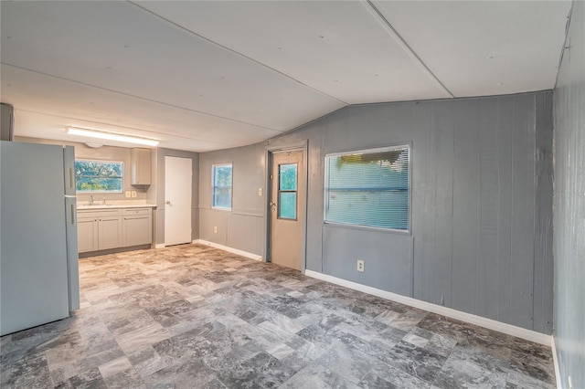 unfurnished room featuring vaulted ceiling, a sink, wooden walls, and baseboards