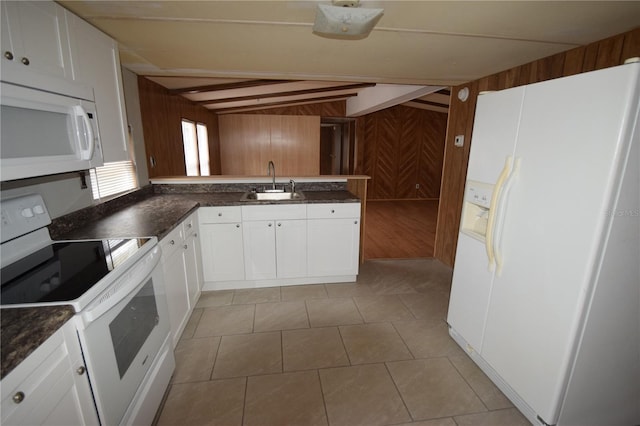 kitchen with white appliances, white cabinetry, a sink, and wood walls