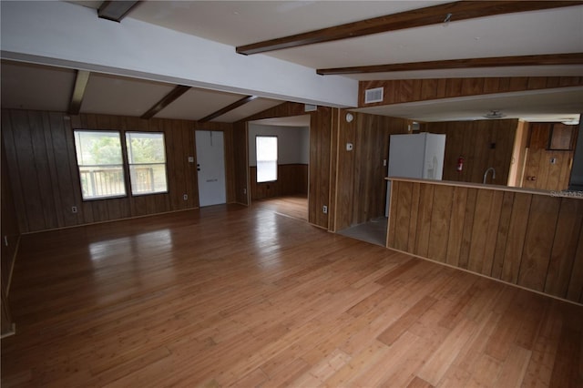 spare room featuring lofted ceiling with beams, wooden walls, visible vents, and wood finished floors