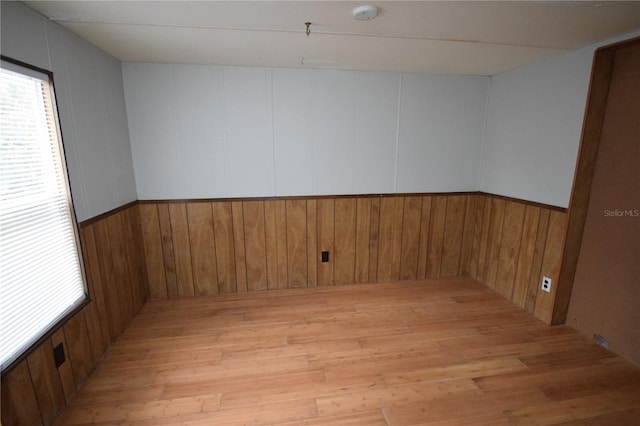 empty room with a wealth of natural light, light wood-type flooring, and wood walls