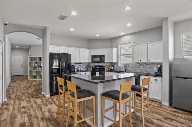 kitchen featuring wood-type flooring, black appliances, a kitchen island, sink, and white cabinetry