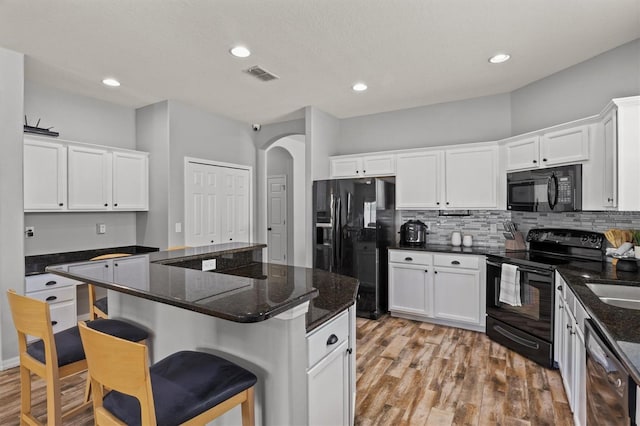 kitchen featuring white cabinets, dark stone counters, and black appliances