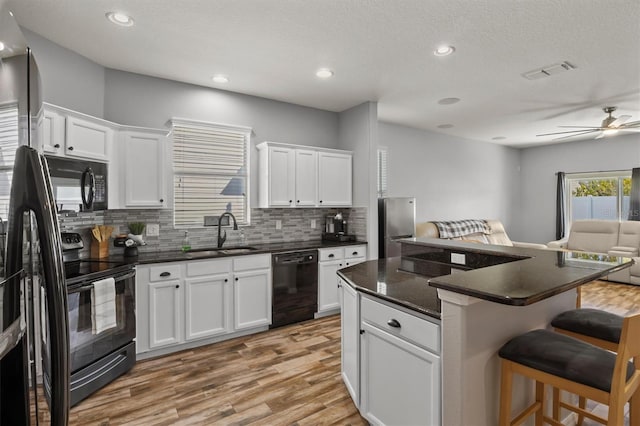 kitchen with white cabinetry, sink, black appliances, and a kitchen breakfast bar