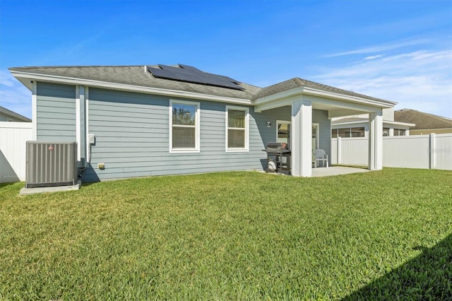 rear view of property featuring central AC unit, solar panels, a yard, and a patio