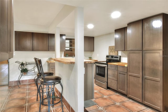 kitchen featuring dark brown cabinets, a kitchen bar, butcher block counters, and stainless steel range with electric cooktop