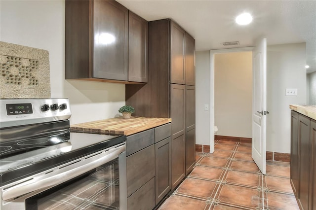 kitchen featuring electric stove, dark brown cabinetry, butcher block counters, and tile patterned flooring