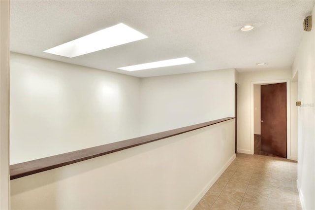 hall with light tile patterned floors, a textured ceiling, and a skylight