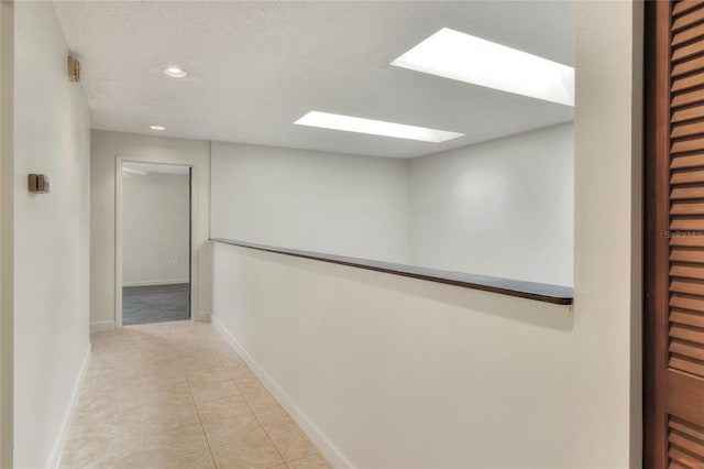 hall with light tile patterned floors, a skylight, and a textured ceiling