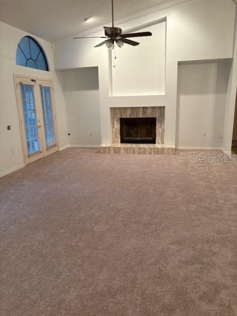 unfurnished living room featuring ceiling fan, high vaulted ceiling, carpet flooring, a fireplace, and french doors