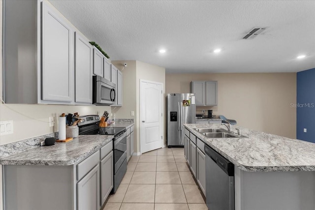 kitchen with light tile patterned flooring, sink, gray cabinets, an island with sink, and stainless steel appliances