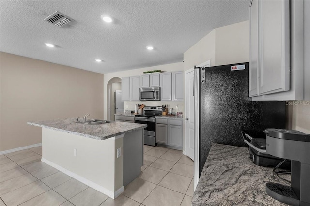 kitchen featuring sink, gray cabinetry, light tile patterned floors, stainless steel appliances, and a center island with sink