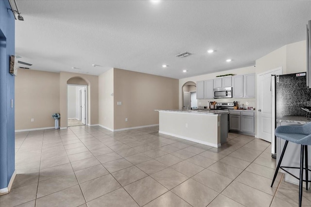 kitchen featuring a breakfast bar, a kitchen island with sink, gray cabinetry, stainless steel appliances, and light tile patterned flooring