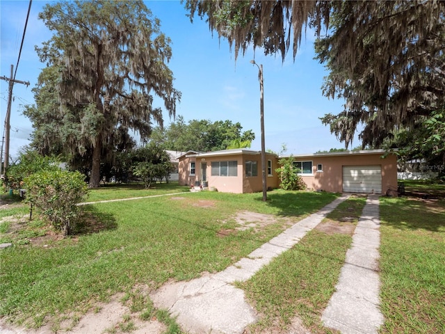 single story home with a garage, driveway, a front lawn, and stucco siding