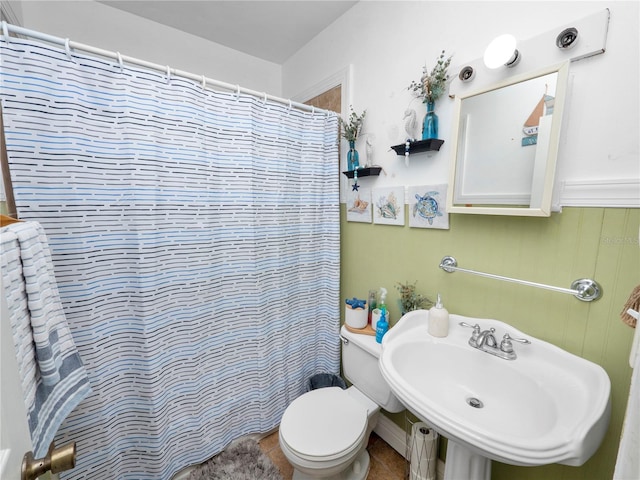 full bath with toilet, curtained shower, a sink, and wainscoting