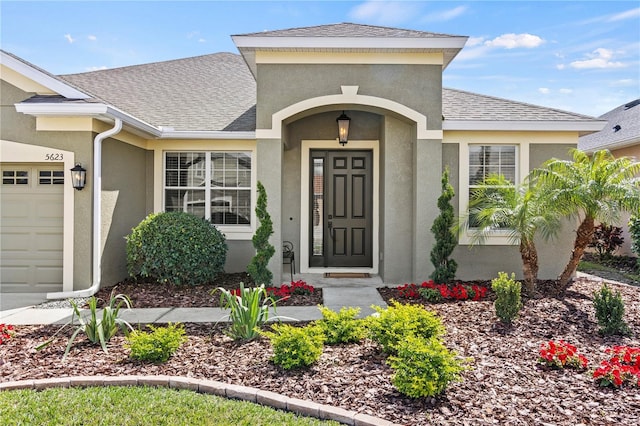 property entrance with a shingled roof, an attached garage, and stucco siding