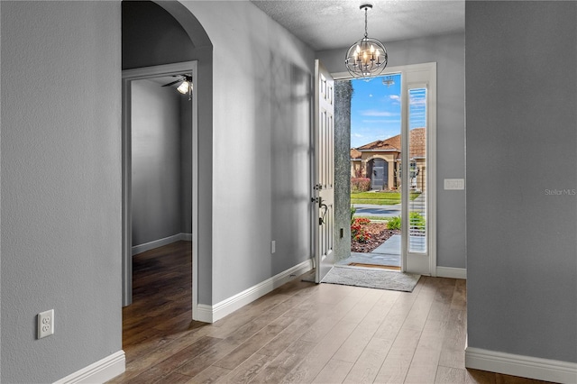 entrance foyer featuring baseboards, arched walkways, wood finished floors, and ceiling fan with notable chandelier