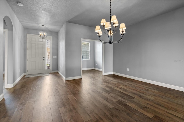 foyer entrance featuring a chandelier, arched walkways, a textured ceiling, dark wood-style flooring, and baseboards