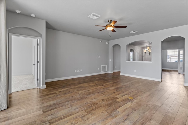 unfurnished room featuring arched walkways, visible vents, wood finished floors, baseboards, and ceiling fan with notable chandelier