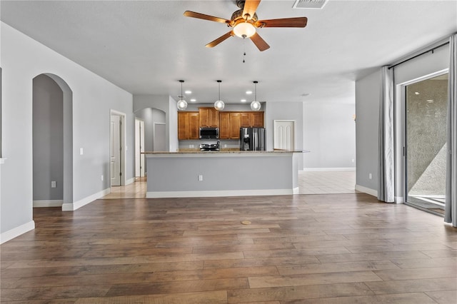 unfurnished living room with arched walkways, ceiling fan, dark wood-style flooring, and baseboards