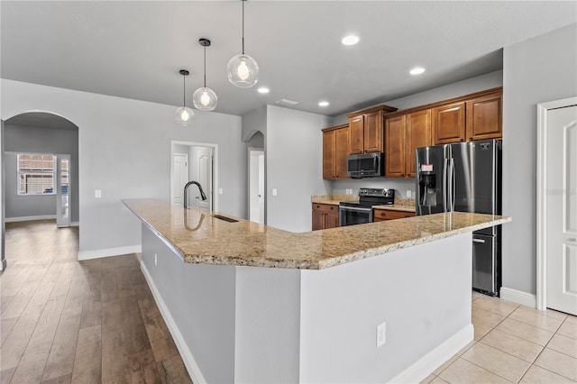 kitchen featuring brown cabinets, a large island, arched walkways, and stainless steel appliances