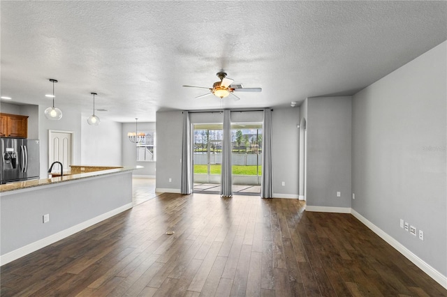 unfurnished living room featuring dark wood finished floors, a textured ceiling, baseboards, and ceiling fan with notable chandelier