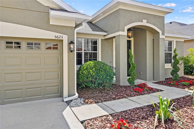 view of exterior entry with a garage, a shingled roof, and stucco siding